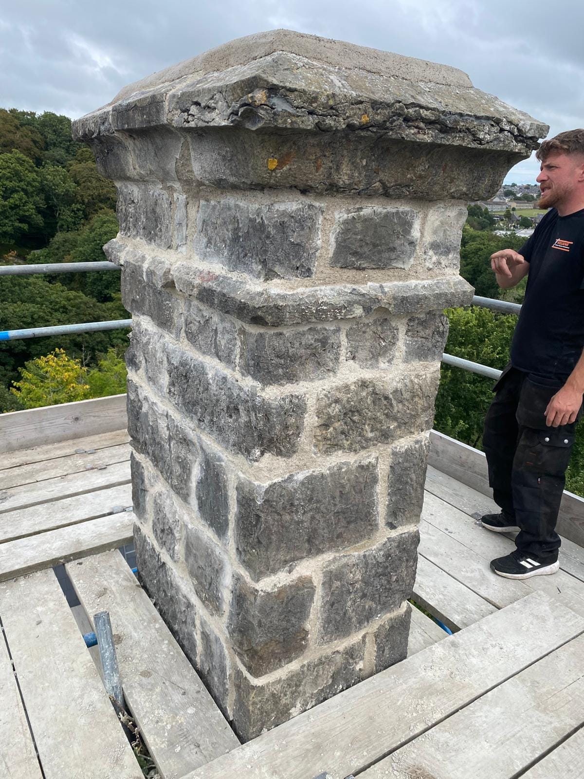 Roofer inspecting weathered chimney stonework during a roof survey